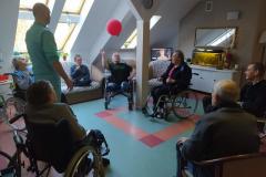 Mieszkańcy na wózkach inwalidzkich z segm. E2 podczas grupowych zajęć usprawniających z fizjoterapeuta odbijanie -balonika